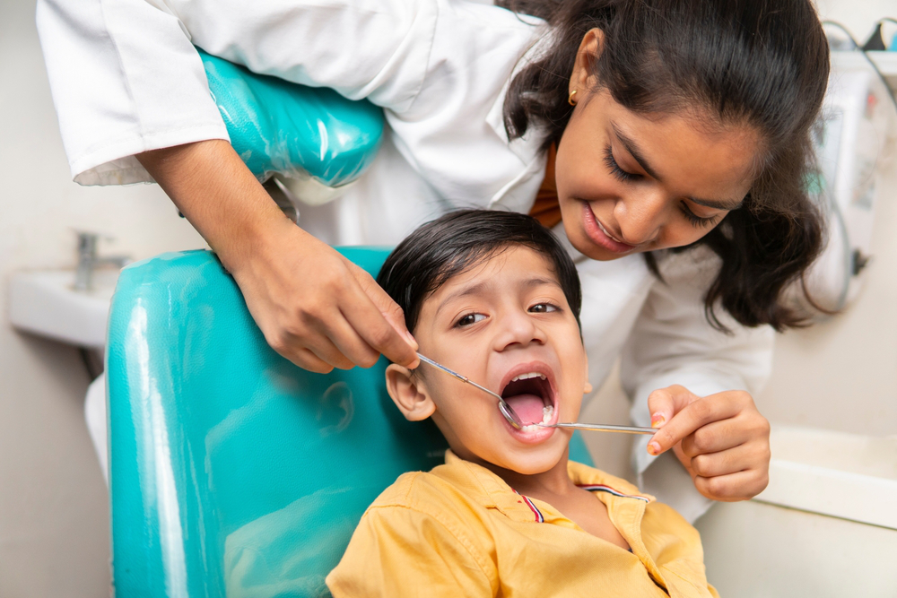 Little boy sitting on the dental chair with open mouth and a female dentist doing his oral checkup at dentist clinic.